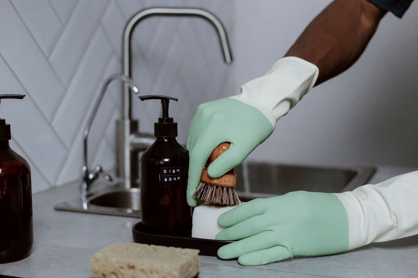 Préposé à l’entretien portant des gants menthe récurant un évier de cuisine