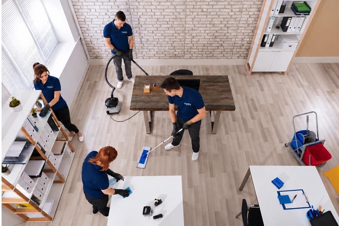 Équipe de Taïdra Cleaning en uniforme marine passant l’aspirateur, la vadrouille et nettoyant les surfaces d’un bureau lumineux